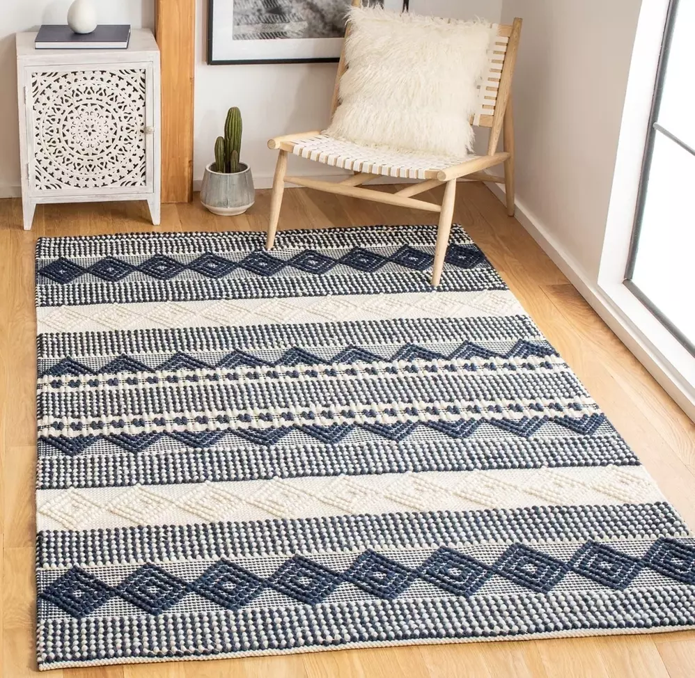 Tapete decorativo azul e branco com padrão geométrico em sala moderna, combinado com cadeira de madeira, planta em vaso e móvel branco com detalhes decorativos.