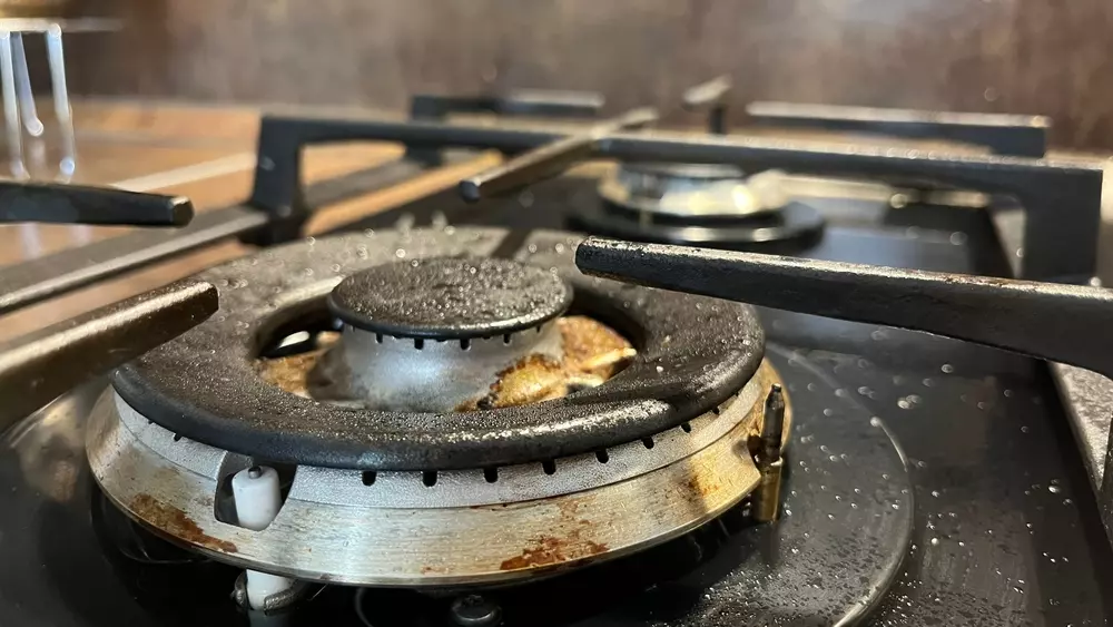 Ângulo aproximado de boca de fogão com resquícios de gordura causados pelo uso.