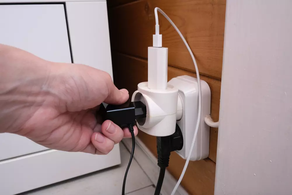 Hábitos perigosos em casa. Mãos de uma mulher colocando diversas tomadas no mesmo adaptador e na mesma extensão elétrica.