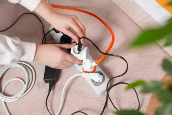 Mãos de uma mulher colocando várias tomadas interligadas e conectadas à uma extensão elétrica. Esse seria um dos hábitos perigosos em casa.