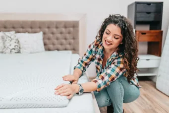 Uma mulher jovem está em uma loja de móveis verificando um colchão que está em cima de uma cama para escolher o melhor item para trocar de colchão em seu apartamento.