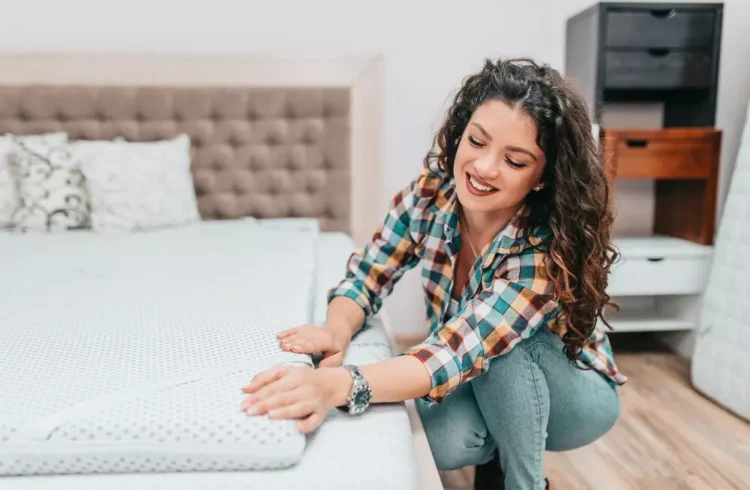 Uma mulher jovem está em uma loja de móveis verificando um colchão que está em cima de uma cama para escolher o melhor item para trocar de colchão em seu apartamento.