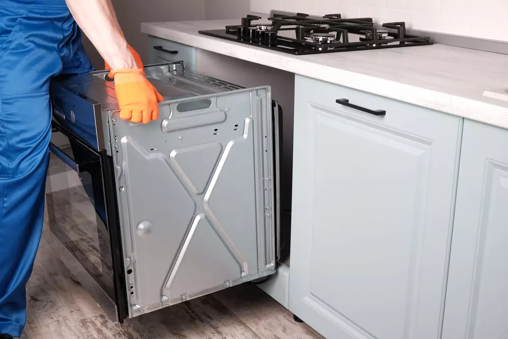 Processo de instalação de forno elétrico em cozinha com mãos de técnico próximo ao eletrodoméstico embutido.