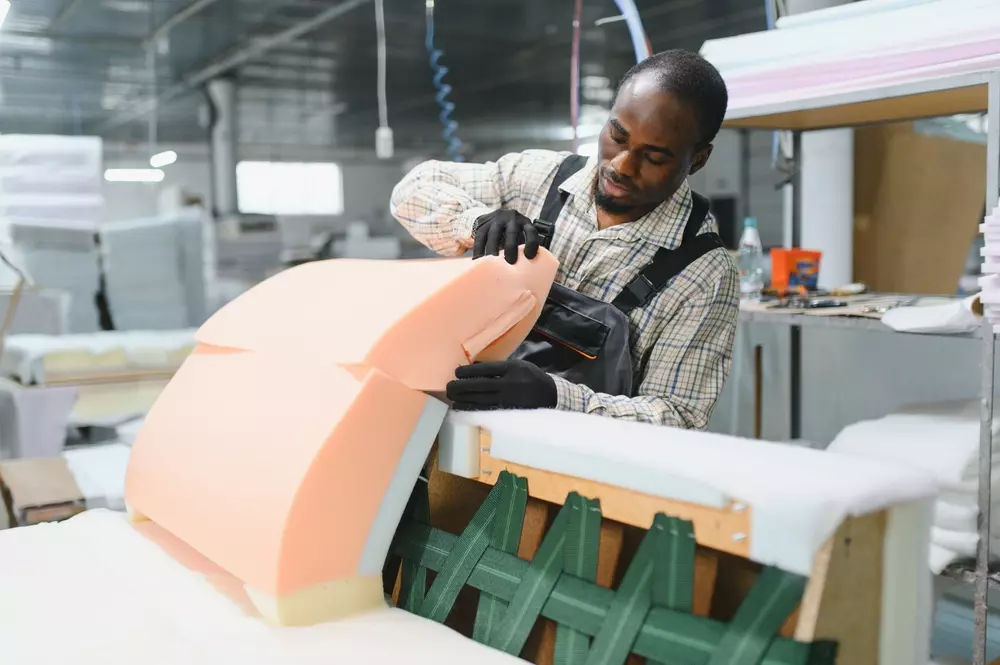Homem trabalhando na fabricação de espuma de alta densidade para sofá, destacando a importância da estrutura e espessura na qualidade do material.