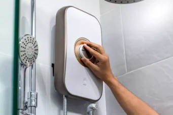 Aparelho de aquecedor de água sendo ajustado na parede do banheiro, próximo ao chuveiro, ideal para aquecer água de forma eficiente.
