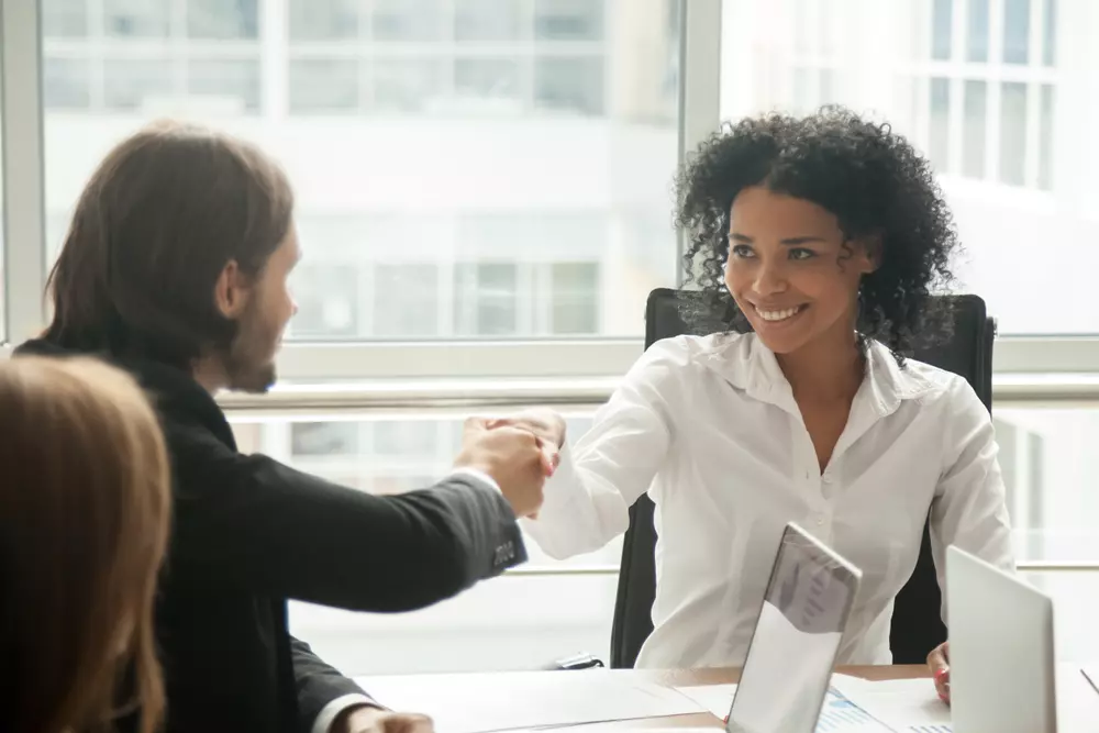 Conversa amigável sobre gestão de condomínio assistida entre uma mulher negra e um homem em um ambiente de escritório, representando diferentes tipos de gestão de condomínios.