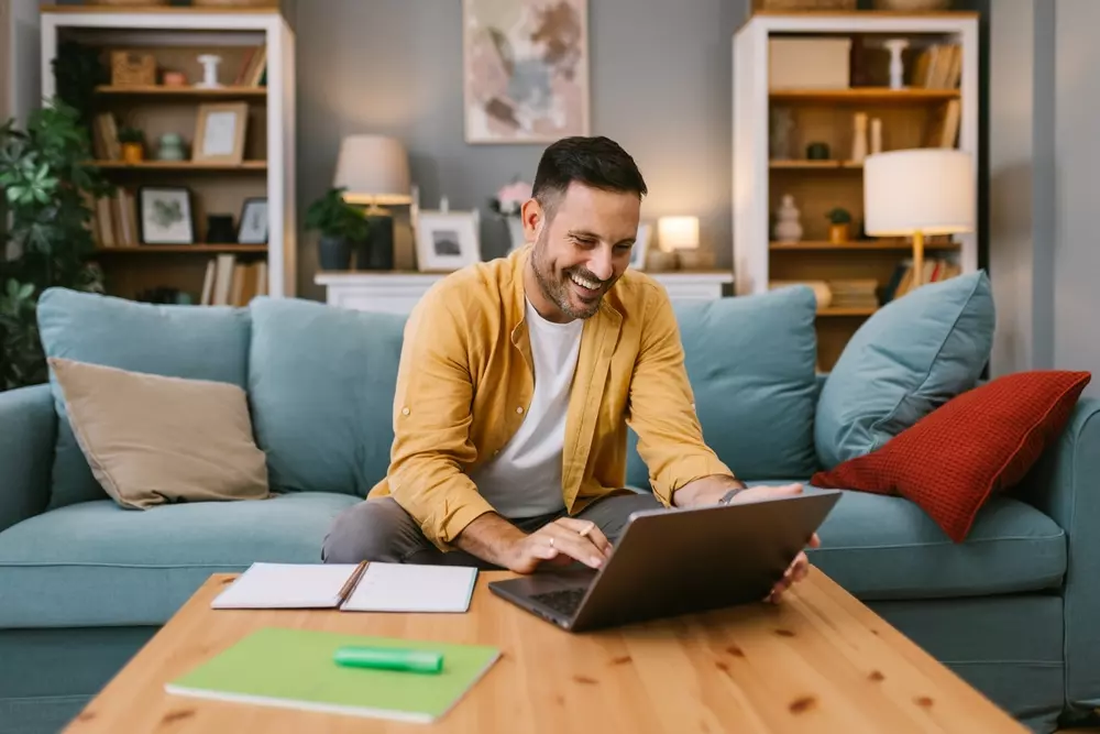 Homem feliz acessando informações sobre tipos de gestão de condomínio e autogestão de condomínios em um ambiente de sala de estar.