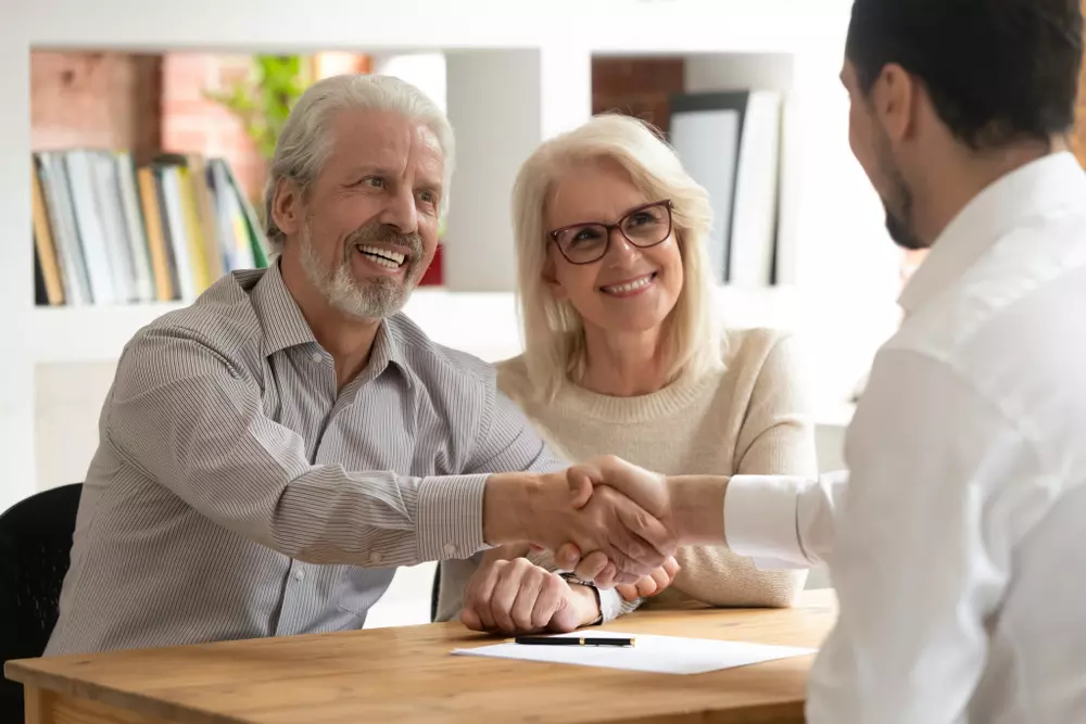 Aposentado e esposa fazendo acordo com representante financeiro, simbolizando a possibilidade do aposentado financiar imóvel com segurança e confiança.