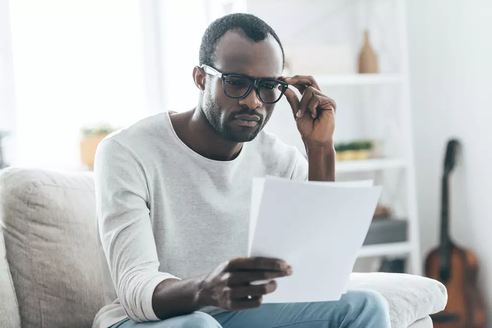 Homem lendo documentos e analisando informações importantes enquanto ajusta seus óculos, representando concentração e atenção.