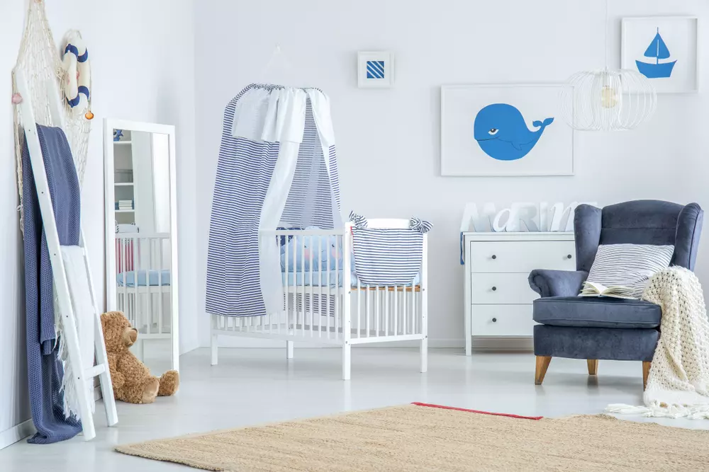 Quarto de bebê com tons de azul, incluindo berço, poltrona confortável e arte nas paredes com desenhos de animais marinhos.