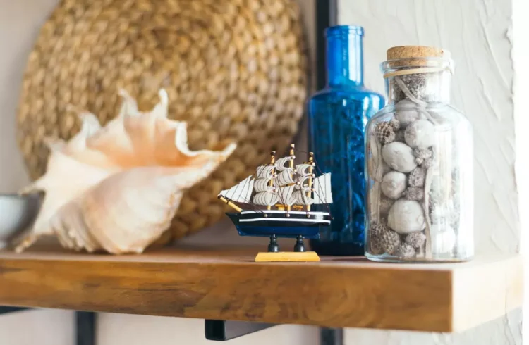Decoração navy com elementos marítimos incluindo concha, barco de navio em miniatura, vidros azuis e recipientes com pedras, criando um toque de mar na decoração da casa.