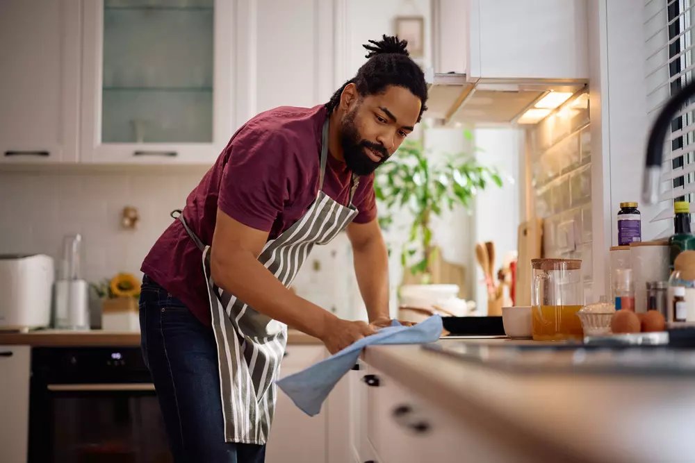 Homem no papel de conscientizar para evitar procrastinar nas tarefas de casa, fazendo a limpeza da cozinha de forma eficiente e organizada, dividindo as tarefas em pequenas doses para manter o foco.