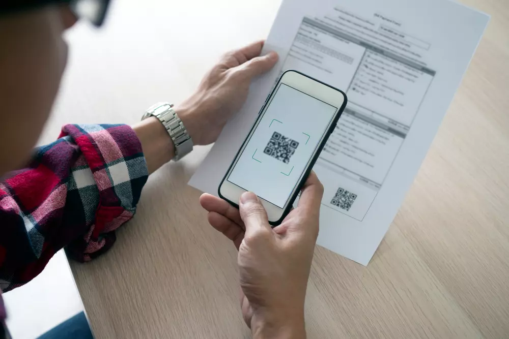 Pessoa analisando documentos relacionados a impedimentos do financiamento com dívidas acumuladas, usando um celular para escanear QR code.