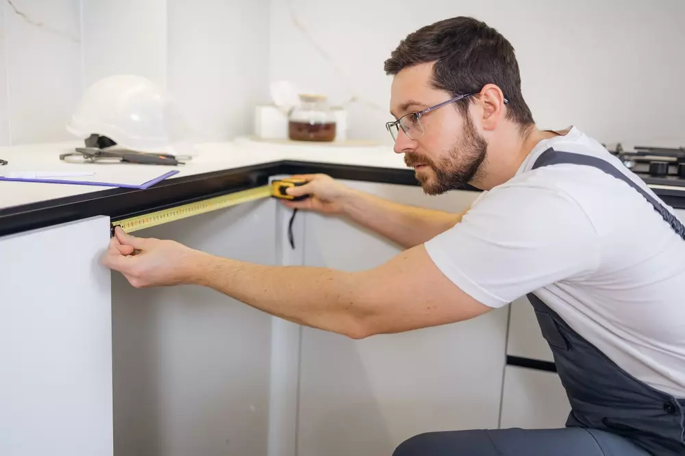 Homem instalando eletrodomésticos embutidos na cozinha, medindo espaço com fita métrica para perfeito encaixe.