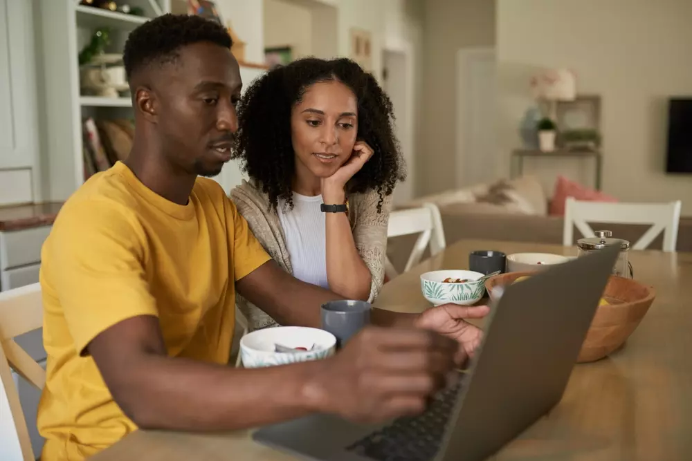 Imagem de um casal olhando para um notebook, planejando suas finanças de forma eficiente e organizada em casa.