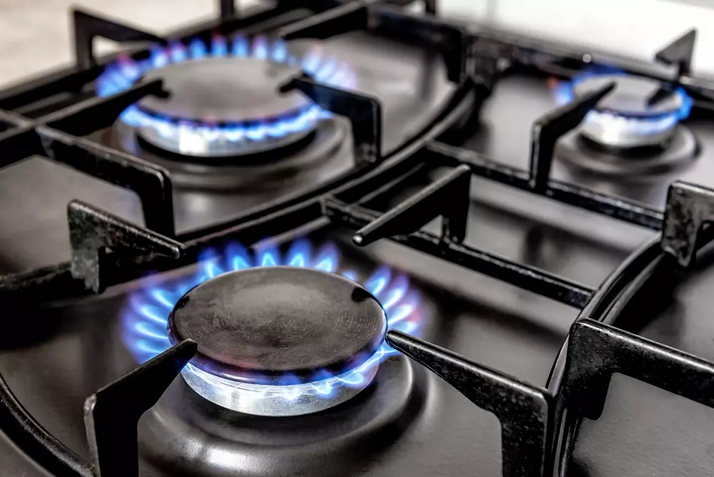 Gás de cozinha acessa uma abertura de fogão a gás, com chama azul brilhante, em destaque para cozinhar ou preparar alimentos.