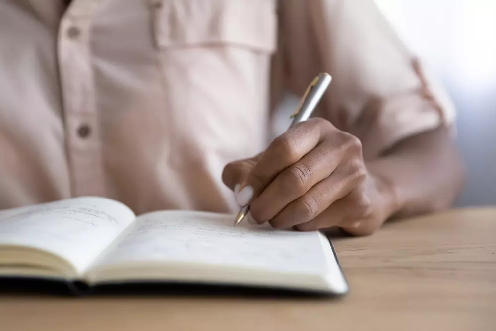 Pessoa anotando tarefas no caderno para evitar procrastinação nas tarefas de casa e manter a organização.