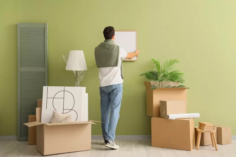 Um homem organizando itens em uma nova residência, preparando-se para a mudança de endereço por motivo de trabalho, com caixas e móveis na sala.