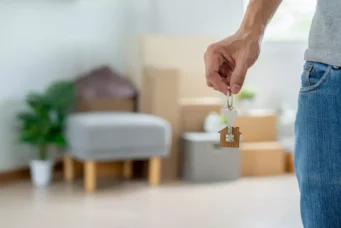 Pessoa segurando chave com pendurador em forma de casa, simbolizando mudança de endereço, ideal para quem busca nova moradia ou transferências de jogador.