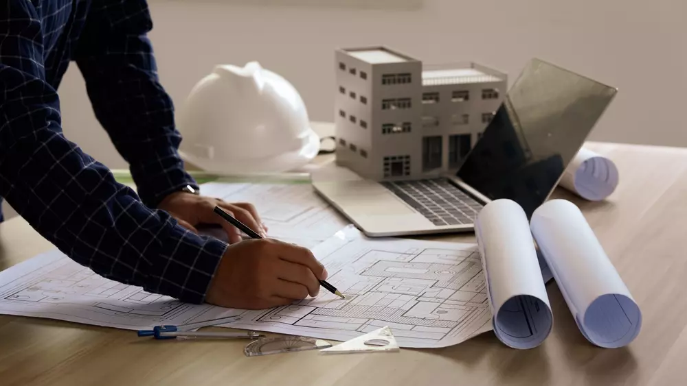 Projeto de engenharia com planos e maquetes de prédio, computador e capacete de segurança, representando garantia estrutural em construções