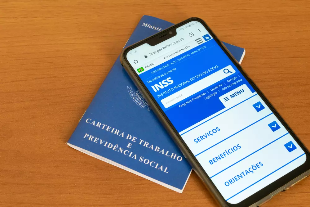 Documentos do INSS e carteira de trabalho na mesa, com celular mostrando site do INSS, indicando opções de financiamento imobiliário para aposentados.