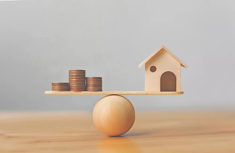 	
Imagem ilustrativa comparando valor de mercado e valor venal do imóvel, com moedas, uma casa de madeira e uma balança de madeira,