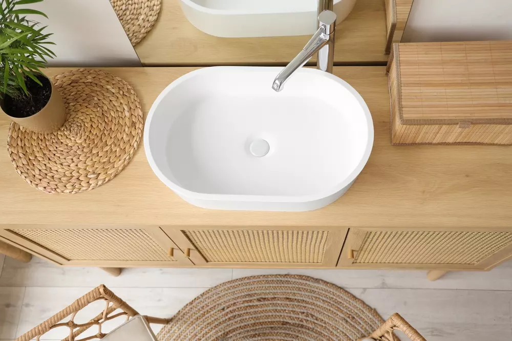 Uma moderna pia de banheiro branca instalada em um móvel de madeira clara, com decoração natural e detalhes elegantes.