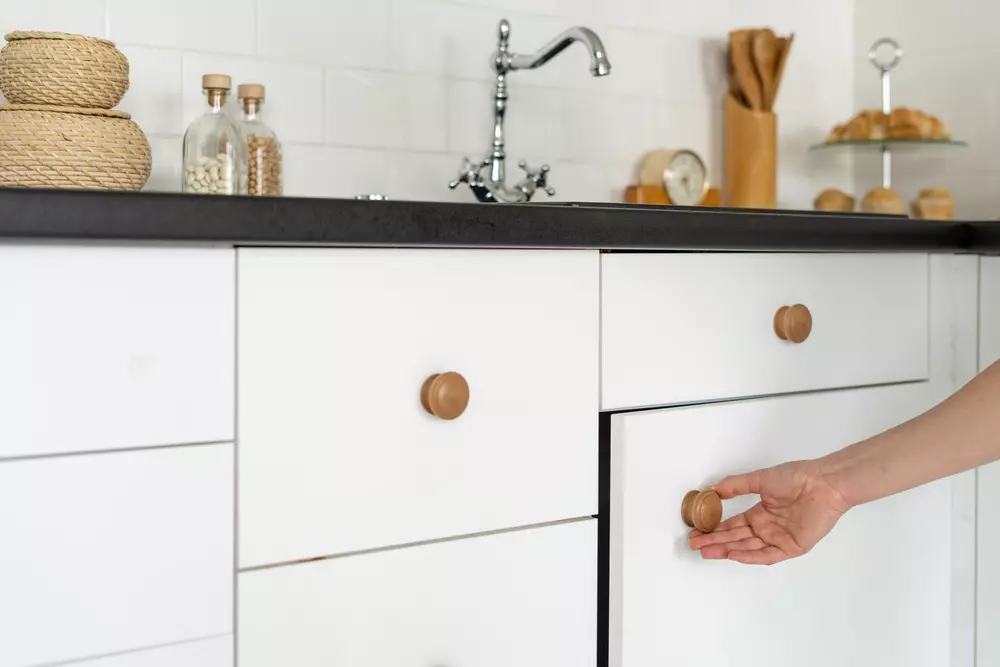 Uma cozinha moderna com armários brancos e gaveta sendo aberta por uma mão, detalhes como utensílios de decoração e pia de aço inox. Ideal para quem busca organização e móveis de cozinha com estilo minimalista.