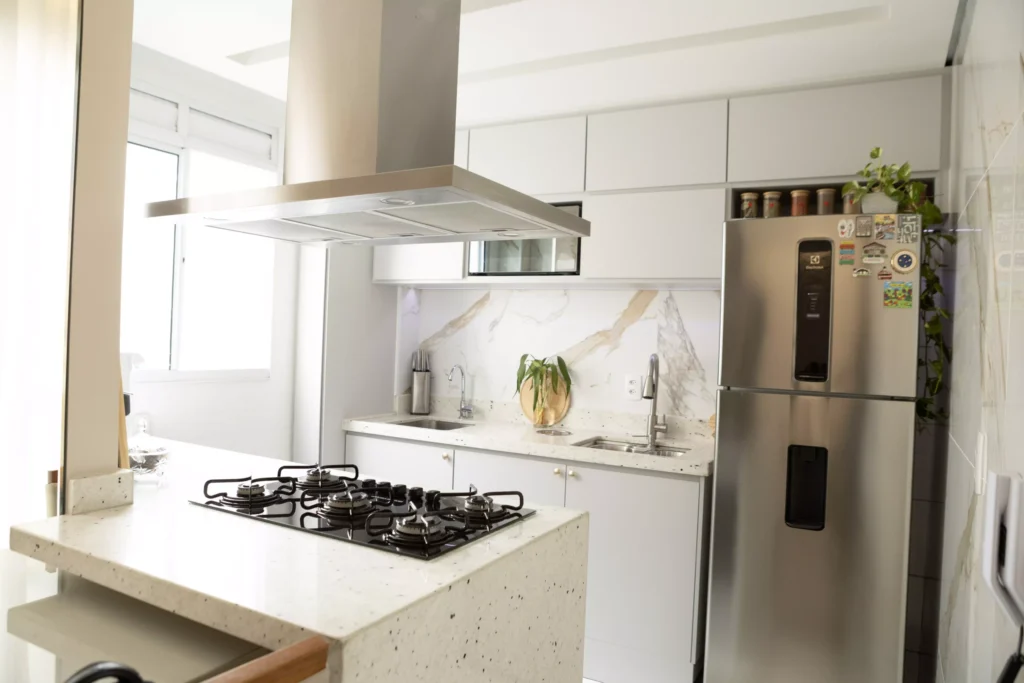 Cozinha moderna e elegante com pia de mármore, fogão de quatro bocas, geladeira de inox, iluminação natural e ambiente perfeito para comprar juntos um imóvel.