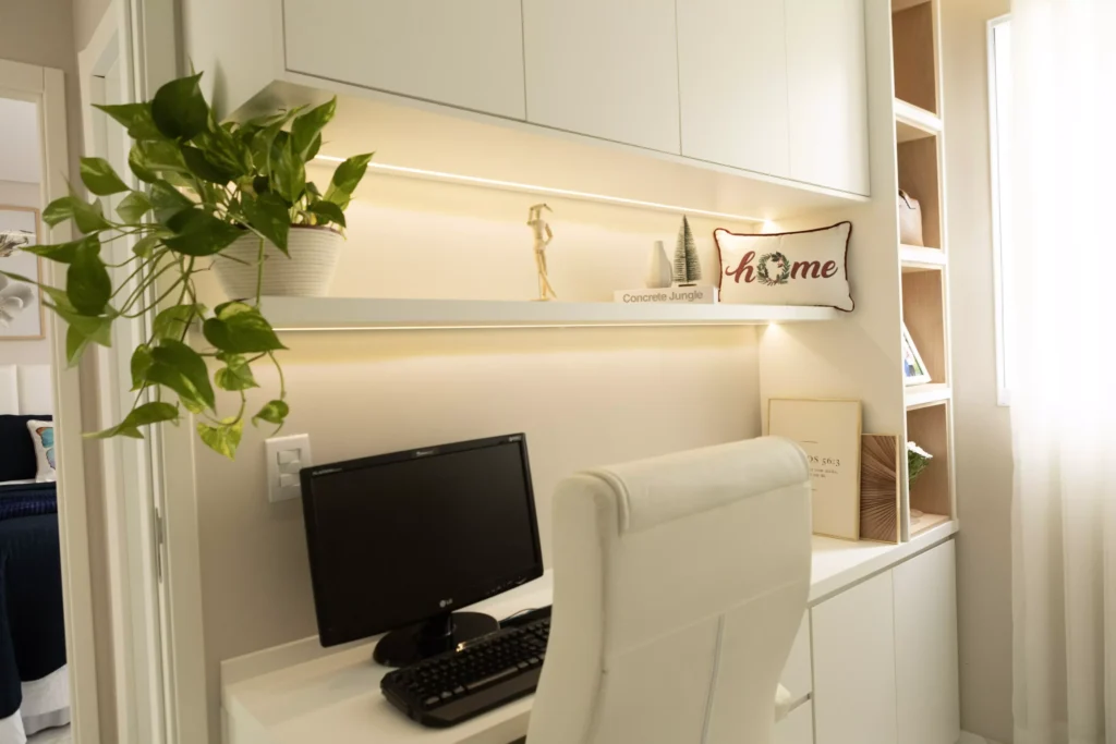 Escrivaninha moderna com computador, prateleiras decorativas, planta verde e iluminação suave, ideal para um escritório em casa confortável e organizado.
