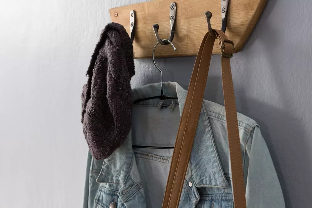 um hanger de roupa na parede com uma jaqueta jeans, um chapéu de tricô marrom e uma bolsa de ombro