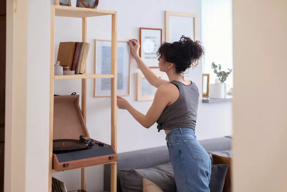 Mulher organizando quadros na parede de casa, cenário com móveis minimalistas e decoração moderna, ideal para quem busca dicas de organização doméstica.