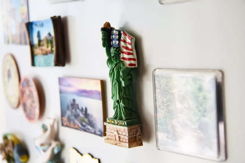 Um miniatura da Estátua da Liberdade comemorativa de Nova York, com detalhes da bandeira dos Estados Unidos, decorando uma parede com outros quadros e objetos afetivos decorativos.