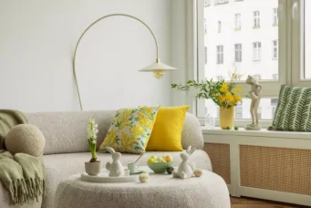 Decoração de primavera na sala com almofadas coloridas, vasinhos com flores, coelhos de cerâmica e elementos decorativos que transmitem a beleza da estação.