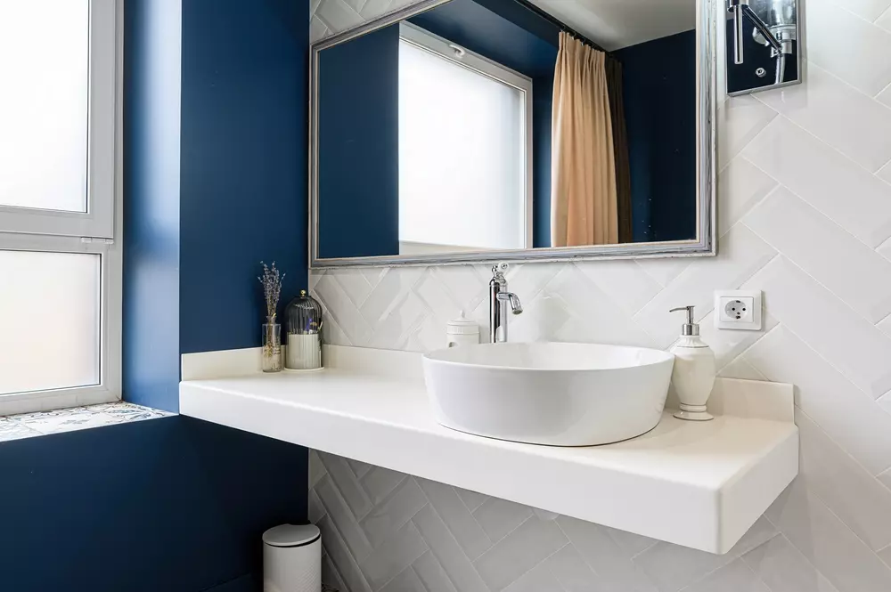 Decorativo banheiro com pia de cuba redonda, espelho grande, parede de azulejos texturizados, vaso sanitário e janela com cortina, ambiente moderno e bem iluminado.