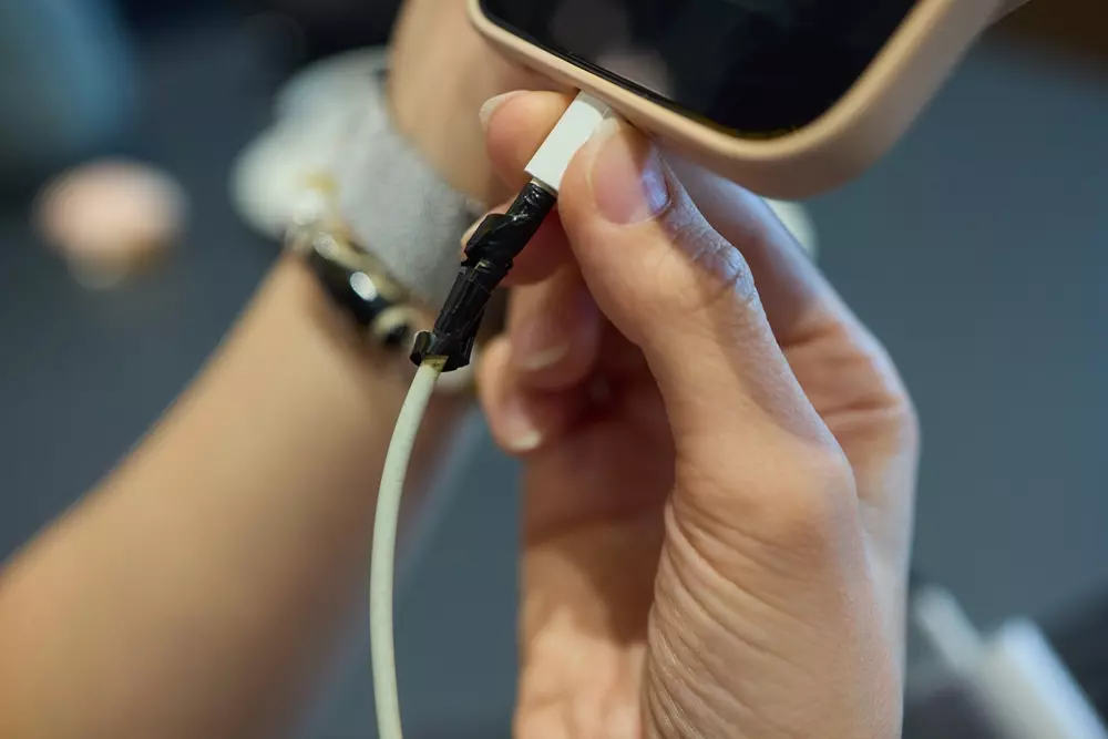 Pessoa segurando um carregador remendado com fita isolante, conectando ao celular para carregamento