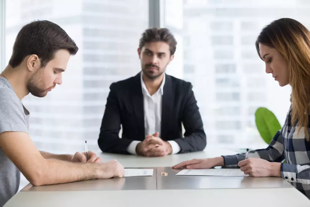 Casal assinando papéis do contrato de compra de seu apartamento, em frente a um advogado.