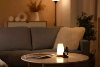 Luminária de abajur de tamanho pequeno sobre uma mesa de canto ao lado do sofá em uma sala de estar aconchegante, com iluminação suave e decoração moderna.