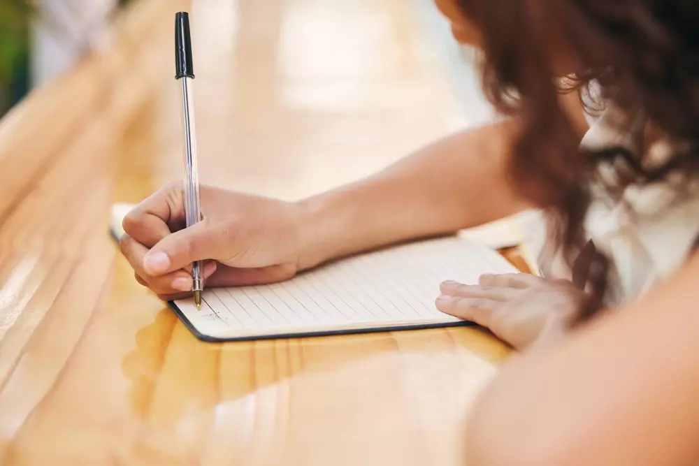 Mulher escrevendo em um diário japonês Kakebo para juntar dinheiro, controlando suas finanças de forma organizada e eficiente.
