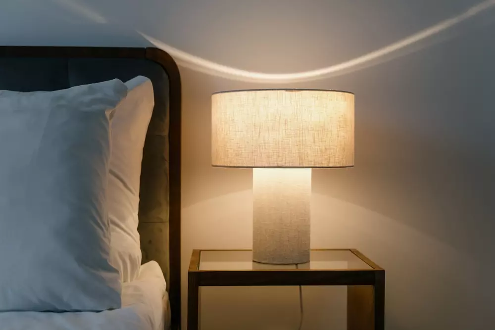 Luz suave e atmosfera romântica em quarto com luminária de tecido e cabeceira de cama ao lado, criando um ambiente acolhedor e romântico para relaxar.