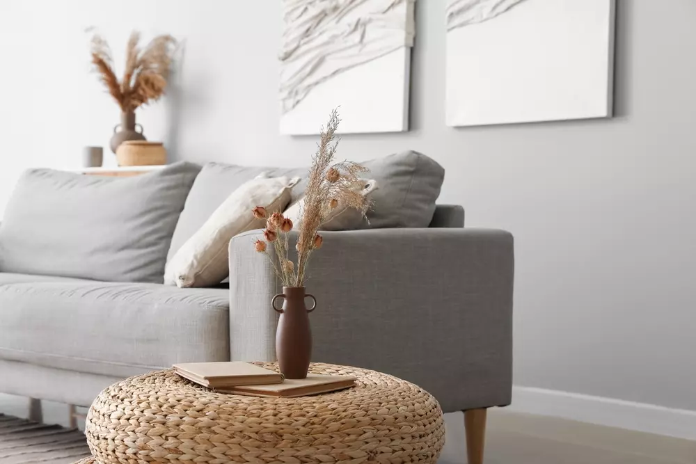 Decoração de primavera em ambiente elegante com vaso de flores secas, sofá cinza, quadros na parede e mesa de fibra natural na sal