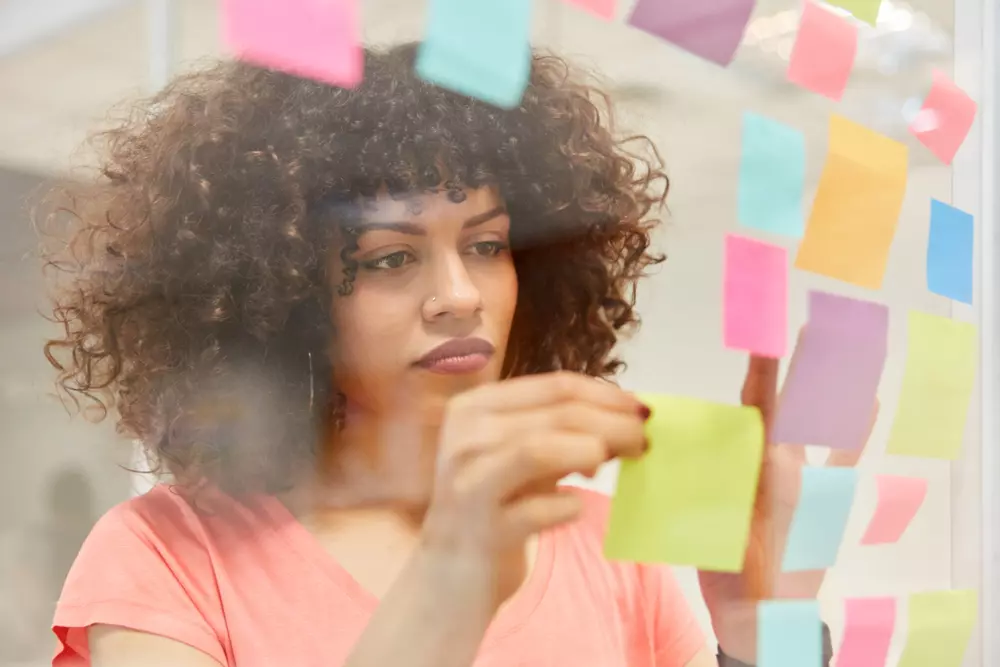 Mulher organizando ideias em notas adesivas para aprender a juntar dinheiro de forma eficiente usando o método smart.
