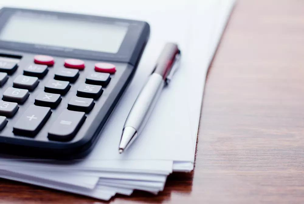 Uma calculadora, uma caneta e papéis sobre uma mesa, representando metodologia DSOP para organização financeira e planejamento.