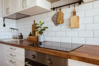 Cozinha moderna com backsplash de azulejos brancos, pia de inox, cooktop de vidro preto e detalhes decorativos em madeira, com o tema 'metro white'