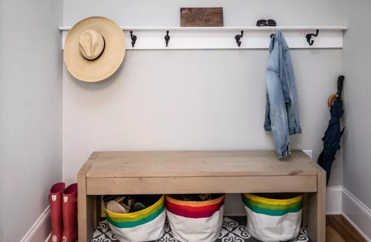 espaço de entrada organizado com ganchos para roupas, uma prateleira superior, uma bancada de madeira e cestos coloridos para armazenamento
