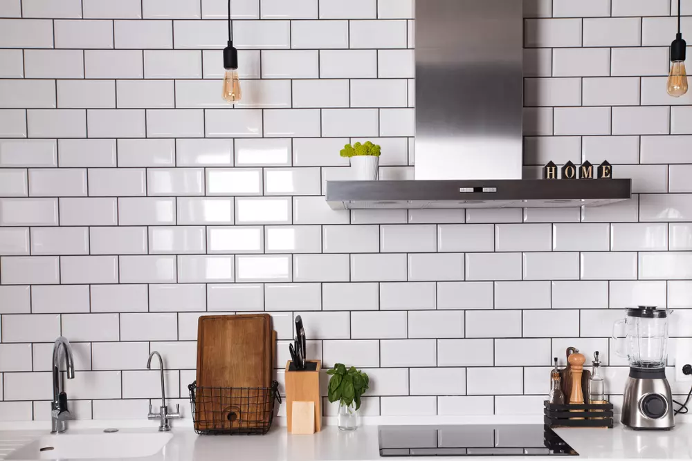 Cozinha moderna com parede de azulejos brancos no estilo metro white, com bancada, utensílios de cozinha e iluminação de pendente.