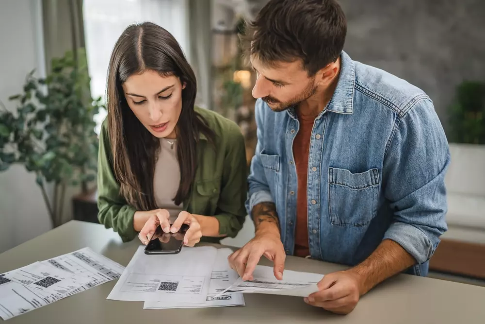 Pessoa explicando a importância de organizar o orçamento para evitar inadimplência no condomínio, com documentos e celular na mesa.