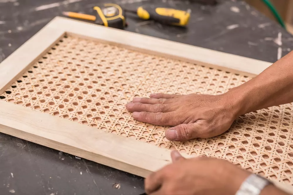 Pessoa trabalhando na fabricação de uma Palhinha Indiana, destacando a diferença no material e acabamento comparado à Rattan.