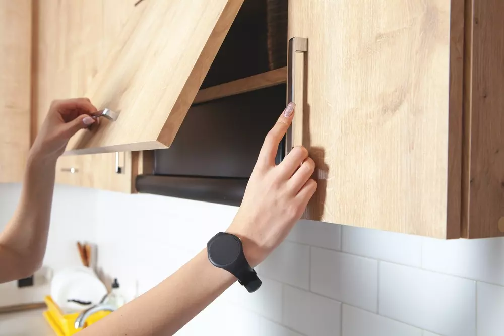 Pessoa abrindo uma porta de armário de cozinha com puxadores modernos de alça em acabamento metálico, destacando o uso de puxadores para mobília.