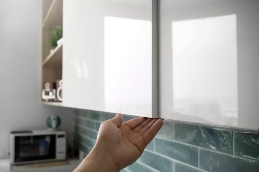 Pessoa abrindo uma porta de armário de cozinha com acabamento branco, em um ambiente moderno e bem iluminado.